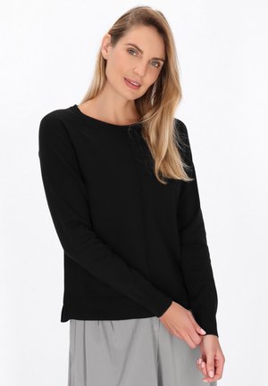Maglione nero con maniche lunghe, scollatura rotonda e polsini a coste. Presenta un design pulito con una texture liscia. Indossato sopra una gonna grigia.