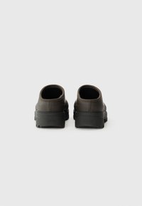 Sötétbarna slip-on cipők kerek hátsó résszel, textúrált gumiburkolattal és vastag fekete talppal. Minimális márkajelzés a sarkon.