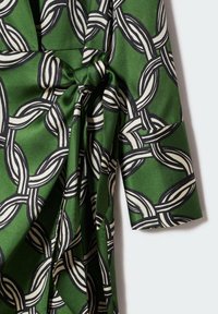 Grüner Stoff mit einem Kettenmuster in Schwarz und Weiß. Das Design umfasst glatte Texturen mit einem geknoteten Detail an der Taille.