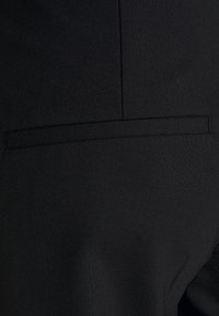 Černé látkové kalhoty s texturovaným povrchem, s malou, plochou kapsou na zadní straně, zdůrazňující čisté linie a štíhlý design.
