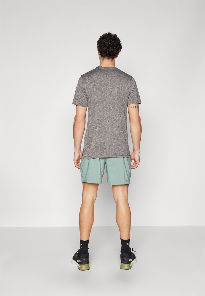 Graues Kurzarm-T-Shirt, hellgrüne Shorts, schwarze Sneakers. Das T-Shirt hat einen Rundhalsausschnitt und eine lockere Passform; die Shorts sind knielang.