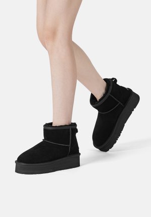 Schwarze Wildleder-Stiefeletten mit einer dicken, strukturierten Sohle. Gefalteter Schaft und kontrastierende Nähte. Kuschelige Fütterung an der Oberseite sichtbar.