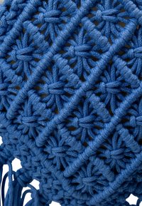 Materiale macramè blu in un motivo a diamante con nodi e frange. La superficie testurizzata con dettagli intricati crea un aspetto decorativo.
