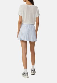 Jupe plissée bleu clair avec ceinture élastique, assortie à un haut blanc à manches courtes. Le mannequin porte des baskets argentées et des chaussettes blanches.