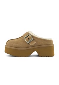 Sabot en daim marron à enfiler avec semelle épaisse, sangle de boucle en métal et doublure en fourrure blanche visible à l'ouverture du talon, présenté sur fond blanc.