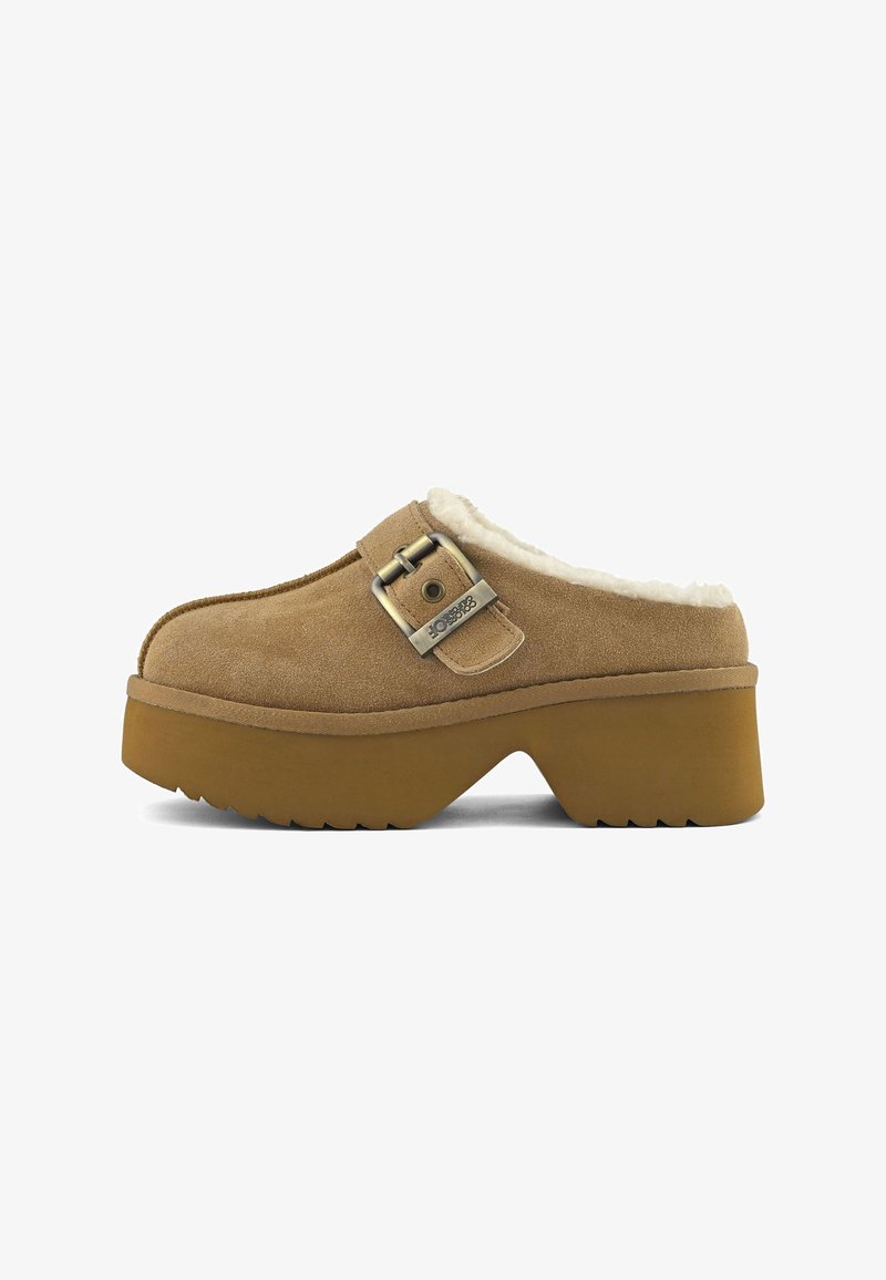 Zoccoli in suede marrone con suola spessa, cinturino con fibbia metallica e fodera in pile bianco visibile all'apertura del tallone, esposti su uno sfondo bianco.