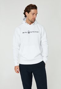 Sudadera blanca con el logotipo "SAIL RACING" en negro. Cuenta con un bolsillo frontal, capucha con cordón y puños y dobladillo acanalados. Textura de tela suave.