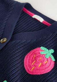 Marineblaues Strickcardigan mit Knopf und einer großen, rosa und grünen gestickten Erdbeerapplikation auf der Brust.