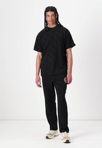 Tricou texturat negru cu mâneci scurte, asortat cu pantaloni negri. Ținuta include o etichetă cu logo pe pantaloni și adidași în culori neutre.