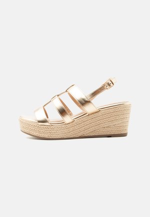 Sandale compensée femme avec brides dorées métalliques et boucle de cheville ajustable, avec une semelle plateforme en jute tissée.