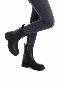 Stivaletti neri alla caviglia in pelle liscia con un design laterale a coste, dotati di una cerniera laterale e di una suola spessa e testurizzata.