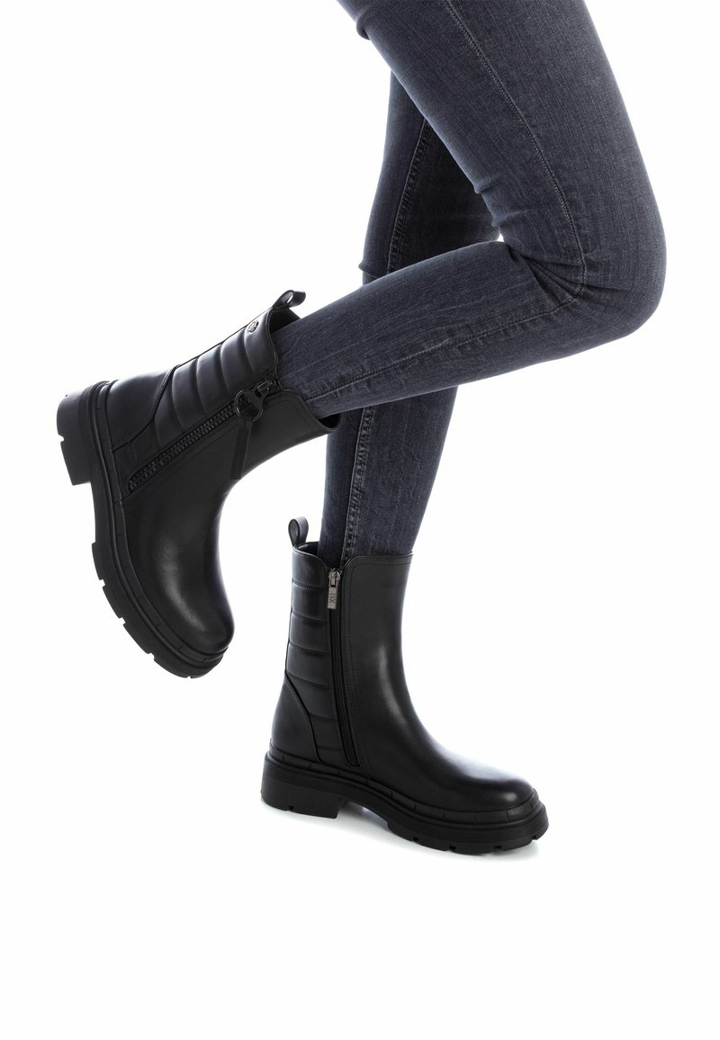 Stivaletti neri alla caviglia in pelle liscia con un design laterale a coste, dotati di una cerniera laterale e di una suola spessa e testurizzata.