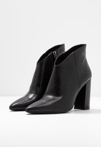 Schwarze Knöchelstiefel mit einem strukturierten Schlangenhautmuster, spitzer Zehenform und blockigem Absatz. Verfügt über einen seitlichen Reißverschluss für mehr Funktionalität.
