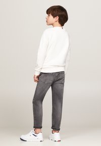 Felpa bianca con colletto rotondo, jeans in denim grigi, e sneakers bianche. Presenta un dettaglio ricamato sul colletto posteriore e maniche arrotolate.