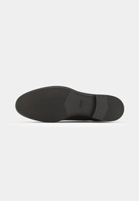 Suola di scarpa in pelle nera con superficie liscia, forma sagomata e grip testurizzato nella punta e nel tallone. Presenta l'impronta del logo del marchio.