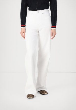 Weiße, hoch taillierte, ausgestellte Jeans mit glatter Textur. Kombiniert mit gemusterten Absätzen im Leopardenmuster.