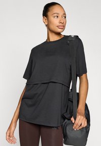 Μαύρο υπερμεγέθες μπλουζάκι με κοντά μανίκια και στρωματοποιημένο σχέδιο. Το κεντημένο ύφασμα ταιριάζει με καφέ κολάν και μια μαύρη τσάντα ώμου.