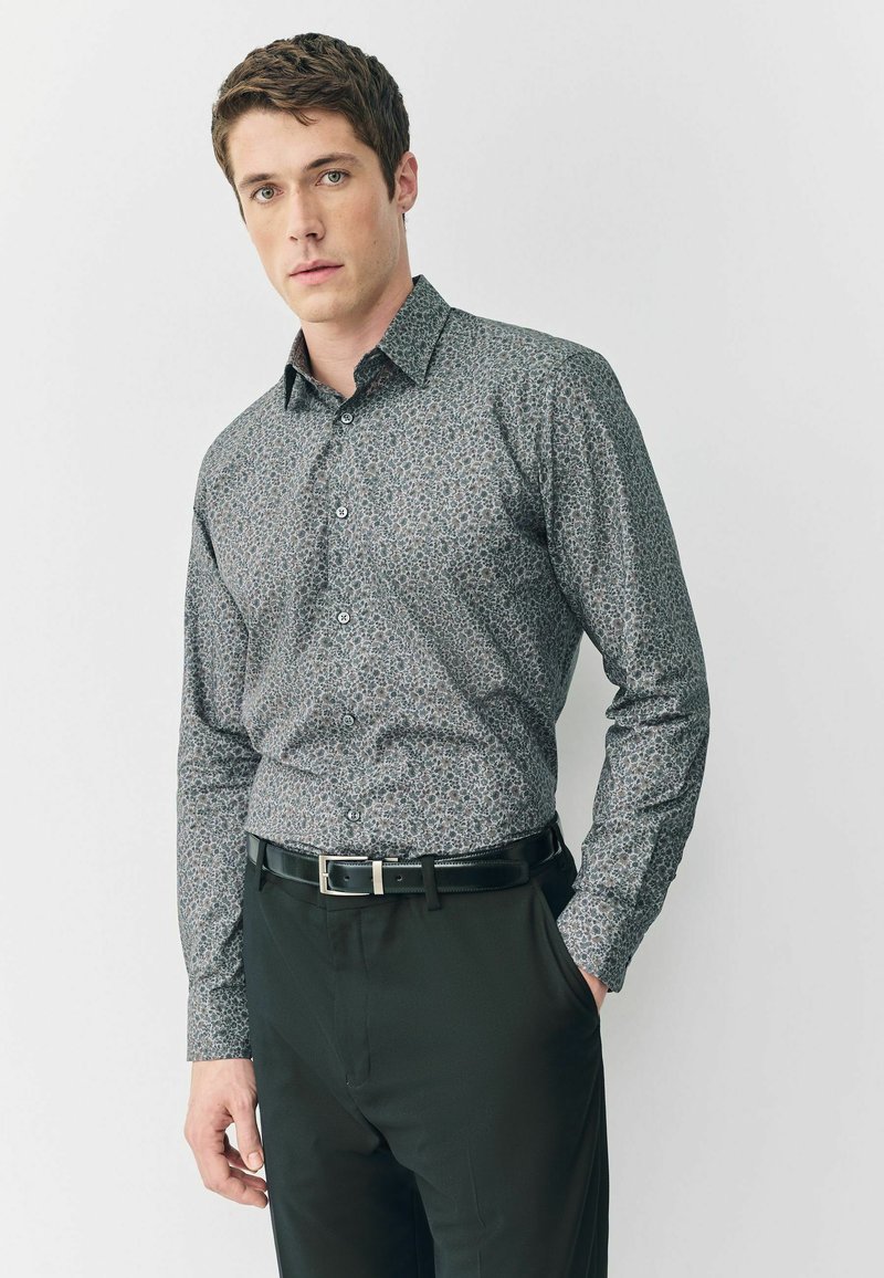 Button-up Hemd in dunklem Blumenmuster, in hellblauen und grauen Farbtönen. Lange Ärmel, Kragen, ergänzt durch schwarze Anzughosen und einen Gürtel.