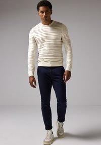 Creme randig stickad tröja, figurnära siluett, rund halsringning; ihop med marinblå slim-fit byxor och beige sneakers med texturerade detaljer.