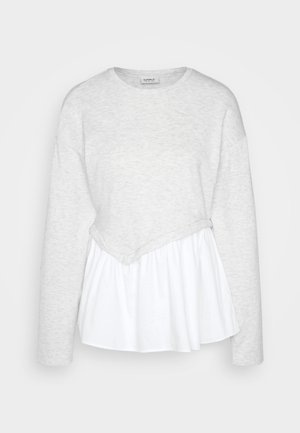 Haut à manches longues gris clair avec un col rond, présentant un design de peplum blanc superposé à la taille et un tissu texturé.