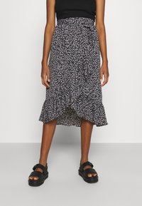 Gonna nera a fiori con motivi rosa e bianchi, orlo arricciato, tessuto leggero e vita aderente, abbinata a sandali neri.