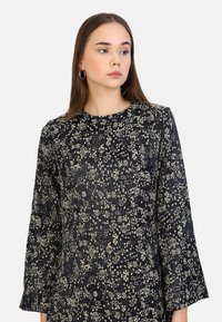 Robe noire à fleurs avec manches longues, présentant un délicat motif de fleurs blanches. Tissu doux avec une texture lisse et décolleté rond.
