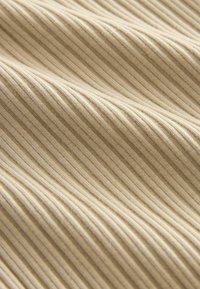 Tejido de color beige con superficie acanalada que presenta finas rayas verticales y una textura suave, mostrando variaciones de luz y sombra a lo largo de la superficie.