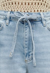 Ανοιχτό μπλε τζιν παντελόνι με δεμένη ζώνη από τζιν στη μέση, σε συνδυασμό με ένα μπεζ πλεκτό τοπ με χαλαρό πλέξιμο.