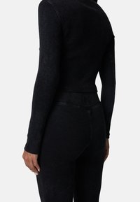 Zwart geribbeld bodysuit met lange mouwen, aangesloten ontwerp en gestructureerde stof. Bevat een naadloze taille en subtiele branding op de achterkant.