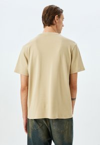 Beige bomulds t-shirt med korte ærmer, rund halsudskæring, glat tekstur og en afslappet pasform. Bådet med blå denim jeans.