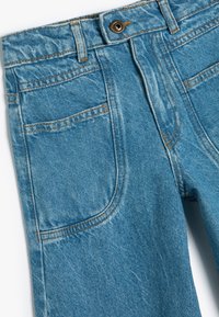 Ljusblå denimjeans med orange sömmar, en framknapp och snedställda framfickor. Slät textur med urblekta partier.