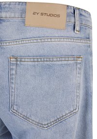 Világoskék farmernadrág hátsó zsebbel és a derékrészen barna bőrcímke "2Y STUDIOS" felirattal varrva.