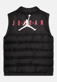 Czarna kamizelka puchowa z wysokim kołnierzem, z wyraźnym białym logo Jumpman i czerwonym napisem "JORDAN" z tyłu. Gładka tekstura.