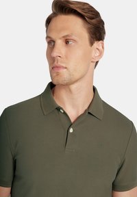 Zielona koszulka polo z krótkim rękawem, wykonana z teksturowanej tkaniny. Posiada miękki kołnierzyk, zapięcie na guziki oraz subtelną aplikację logo na piersi.