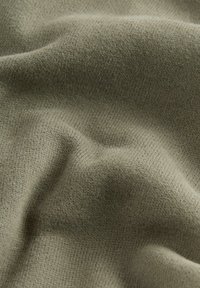 Tissu tricoté doux et beige avec une texture fine visible et de douces plis créant des ombres et des reflets subtils.