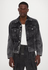 Jachetă din denim negru cu un finisaj texturat, două buzunare pe piept, nasturi tip snap și un guler clasic. Purtați peste un tricou alb.