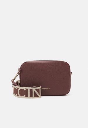 Rechthoekige donkerbruine leren crossbodytas met een textuurrijk oppervlak en een beige stoffen band met grote bruine Coccinelle-logo.