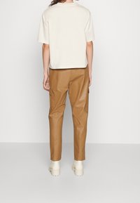 Cremefarvet kortærmet skjorte i afslappet pasform, parret med tan-farvet faux læder cargo bukser med sidelommer og tapered ben. Beige ankelstøvler.