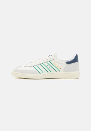 Baskets blanches Adidas Spezial avec des bandes vertes, lettrage doré, semelle crème et talon bleu foncé, vues de profil sur fond uni.
