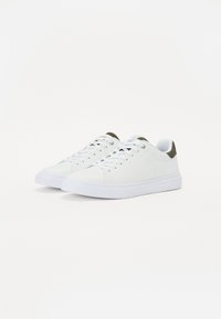 Lave hvite sneakers med hvite snører og mørkegrønne polstrede hælkoller, plassert side om side på en hvit bakgrunn.