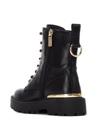 Bota de cuero negro hasta el tobillo con herrajes dorados, cremallera lateral, suela robusta y cordones decorativos. Presenta una entresuela con detalles dorados.