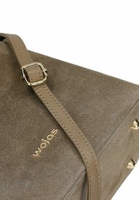 Taupe Wildlederhandtasche mit verstellbarem Lederträger, goldener Schnalle, goldenem "wojas" Logo und goldenen Metallfüßen an der unteren Ecke.