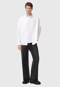 Camisa blanca de botonadura, jeans negros de pierna ancha y zapatos negros. La camisa tiene una textura suave y los jeans presentan un patr�ón ligeramente desgastado.