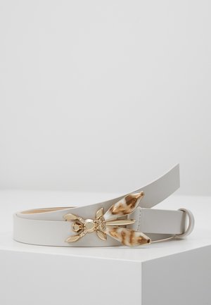 Witte leren riem met een gouden en schildpadvormige insectgesp, rustend op een wit oppervlak tegen een effen achtergrond.