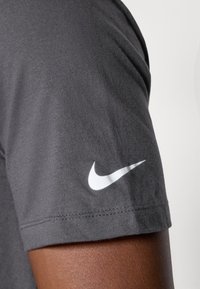 Grå bomulds T-shirt med et hvidt Nike swoosh logo på den venstre ærme. Stoffet har en glat tekstur og en tætsiddende design.