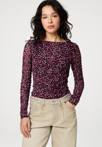 Langarmoberteil aus durchsichtigem schwarzem Mesh mit einem floralen Muster in Pink und Orange. Verfügt über einen Bootausschnitt und eine geraffte Textur. Kombiniert mit beigen Hosen.