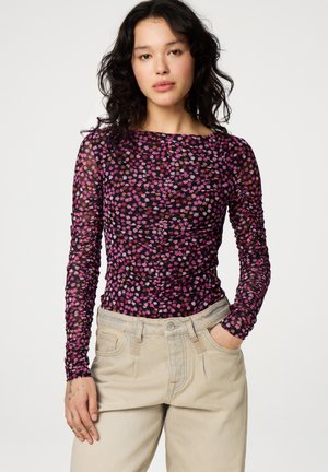 Langarmoberteil aus durchsichtigem schwarzem Mesh mit einem floralen Muster in Pink und Orange. Verfügt über einen Bootausschnitt und eine geraffte Textur. Kombiniert mit beigen Hosen.