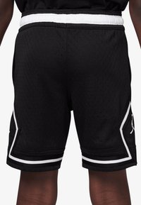 Black mesh athletic shorts with a white elastic waistband, featuring side pockets, white accents, and a logo on the lower left side.