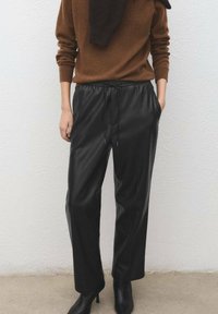 Black leather pants with a loose fit, featuring an elastic waistband and drawstring. Paired with a brown knit sweater and black heeled boots.