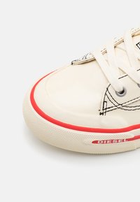 Vita lädersneaker med röd gummisula, kontrasterande sömmar och en logoetikett. Har runda öglor och platta skosnören.